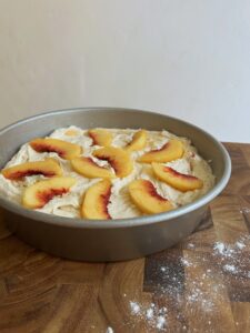 Peach slices arranged in a circular pattern on top of the peach cake batter in the pan.