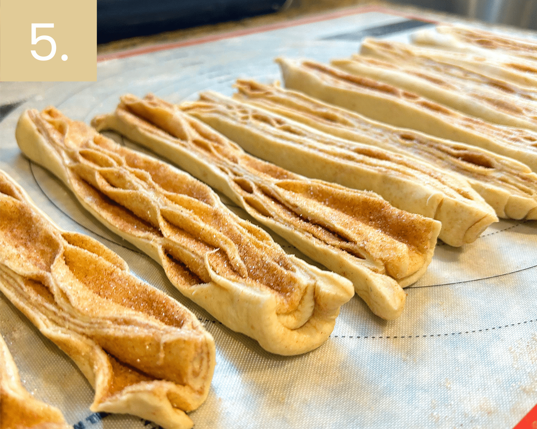 Cutting rolled dough into long strips to reveal flaky cinnamon sugar layers.