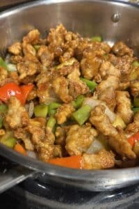 Orange chicken and vegetables cooking in a saute pan on the the stove.