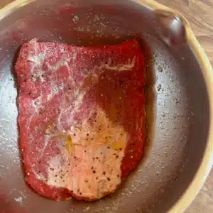 marinating flank steak in a bowl with olive oil and steak seasoning