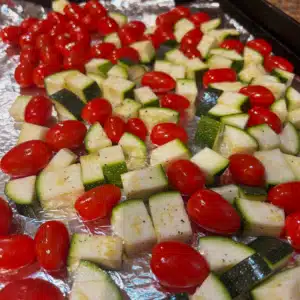 Chopped zucchini and cherry tomatoes on a sheet pan lined with foil, tossed in olive oil, salt, and pepper.