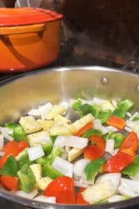 Green Bell Pepper, red bell pepper, pineapple, and white onion cooking in a pan on the stove.
