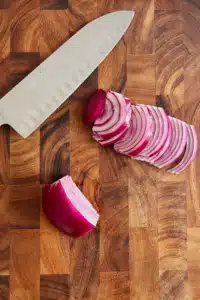 Thinly sliced red onions on a cutting board with a knife