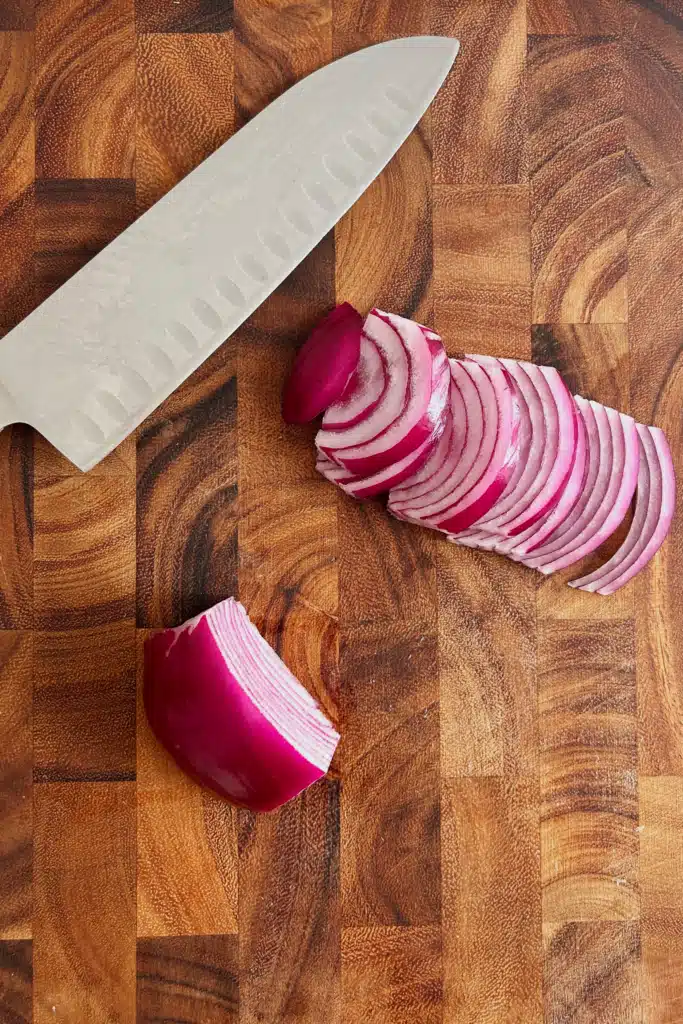 Thinly sliced red onions on a cutting board with a knife