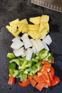 Diced pineapple, white onion, green bell pepper, and red bell pepper on a cutting board.
