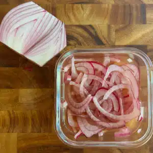 sliced onions in a glass container with apple cider vinegar.