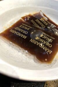 Orange sauce packets warming in a bowl with hot water.