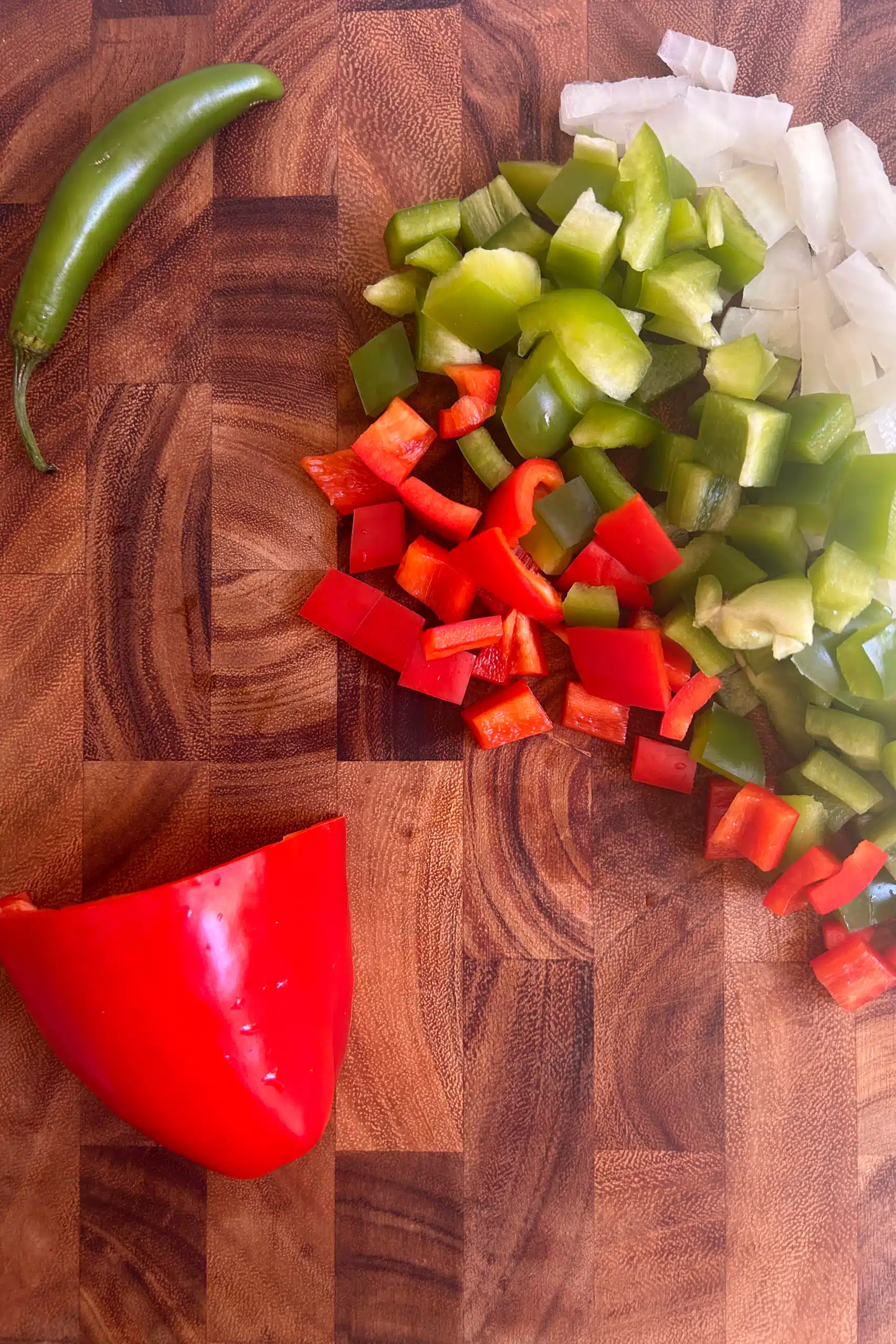 Diced red bell pepper, green bell pepper, and onion on a cutting board.